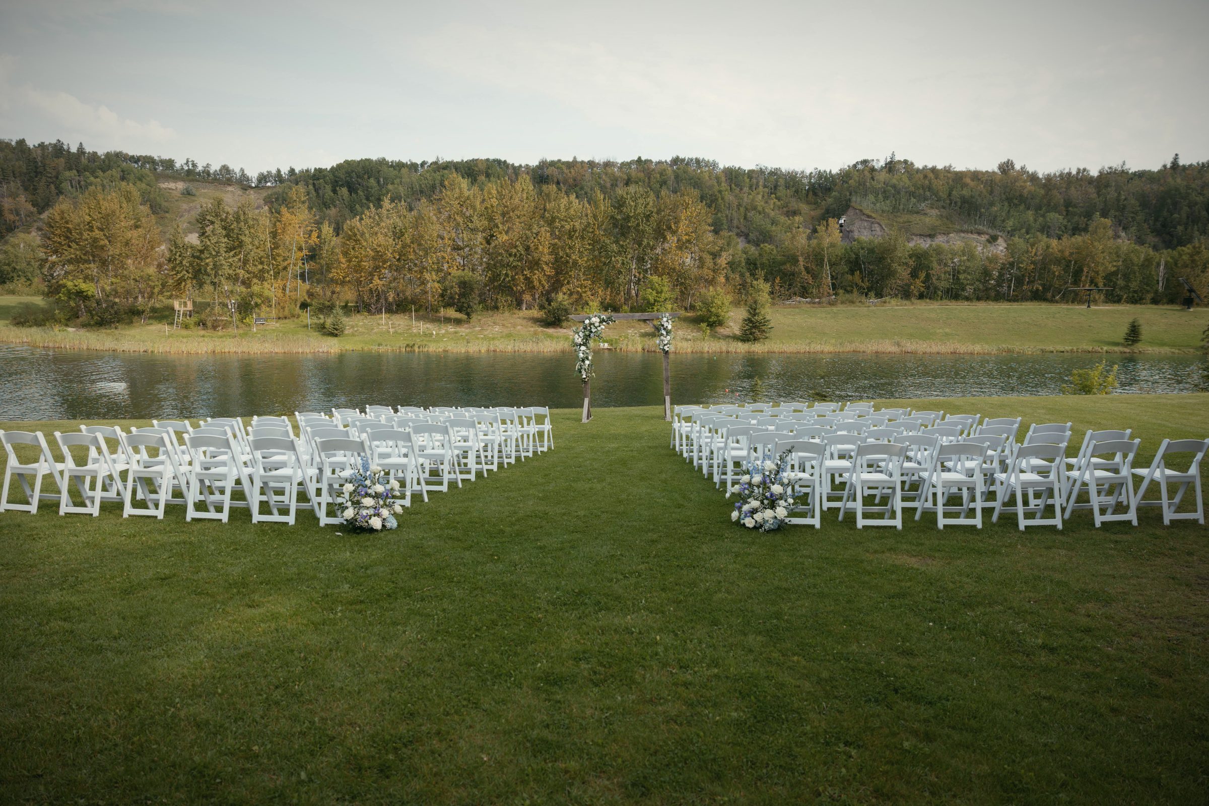Rows of white chairs set on the grass at the water's edge, the lake beyond