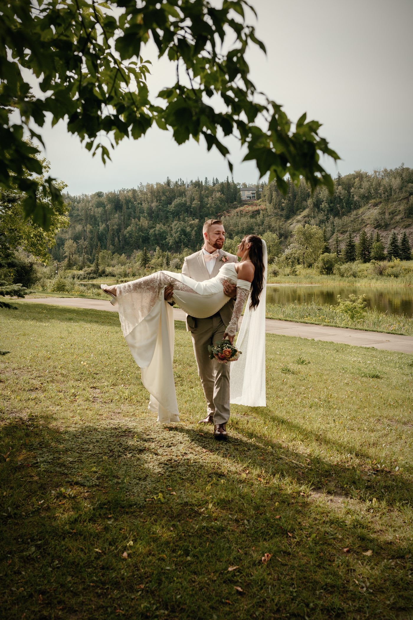 The groom carrying his bride across the lawn beneath an old tree