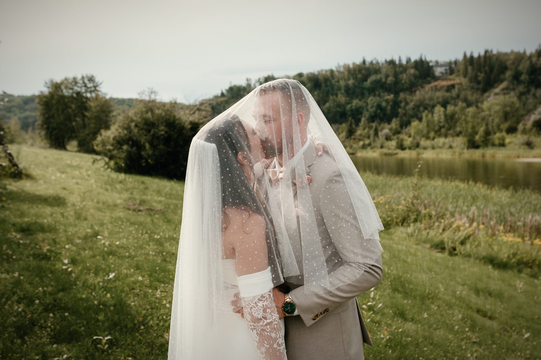 A couple hidden beneath a veil on the hillside, the lake behind