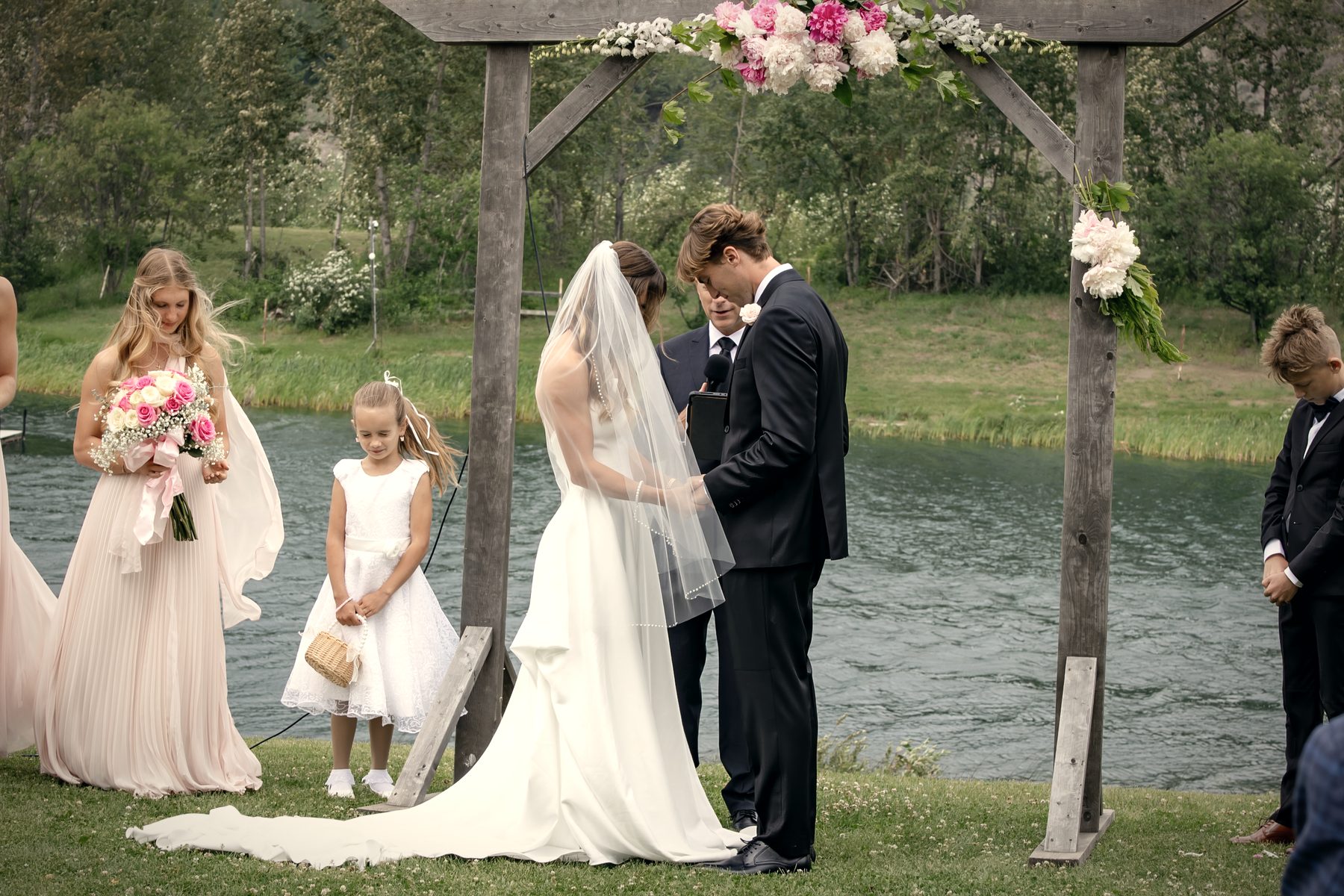 Vows at the flowered arbour, a flower girl at the bride's side and the lake behind