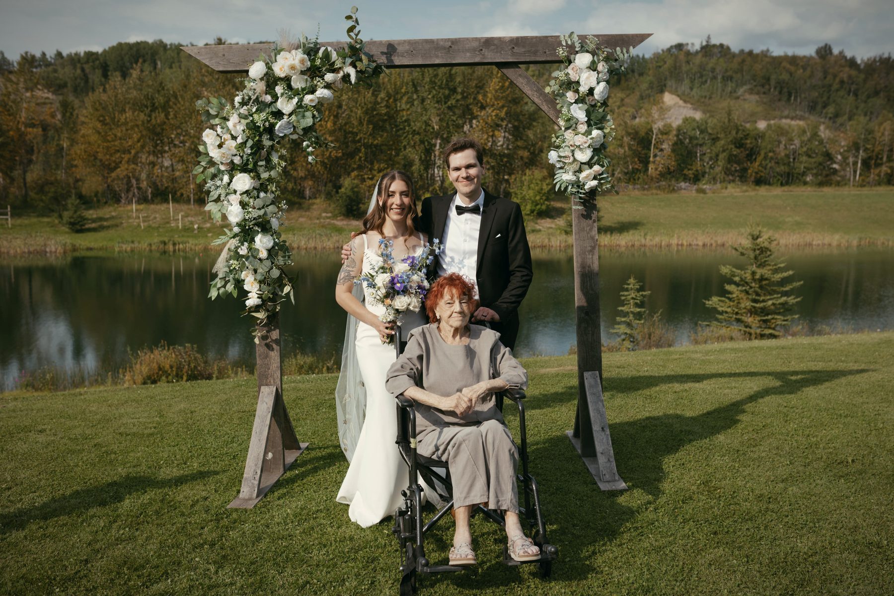 A couple at the flowered arbour beside the lake, an older woman seated in a wheelchair beside them