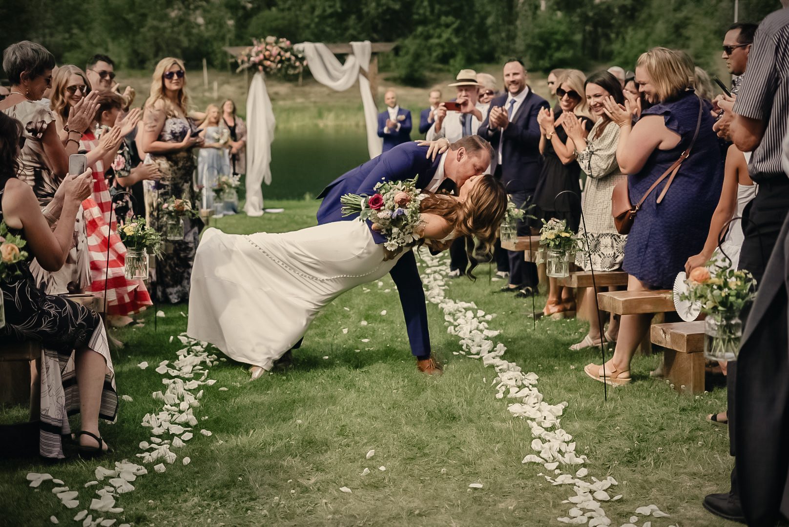 The groom dipping his bride in the aisle, guests laughing and cheering on both sides