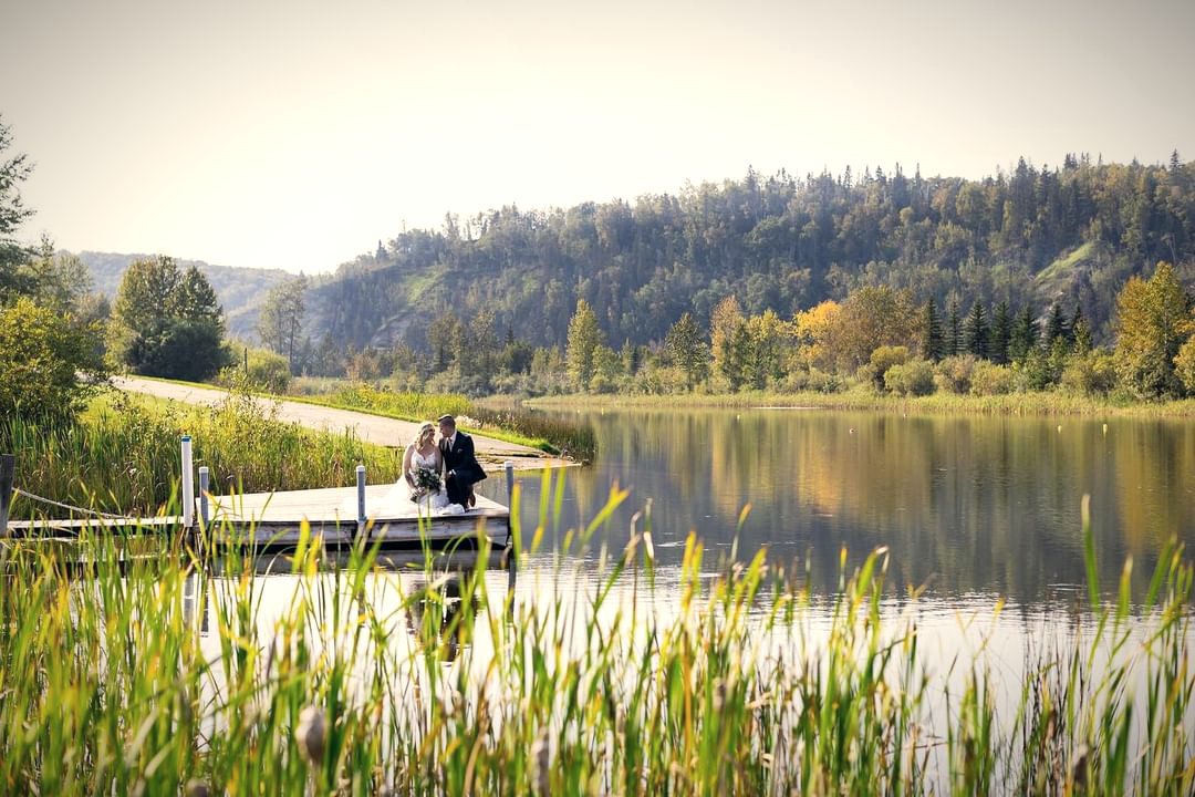 A couple standing at the end of the dock, small in the distance, the lake and reeds in the foreground