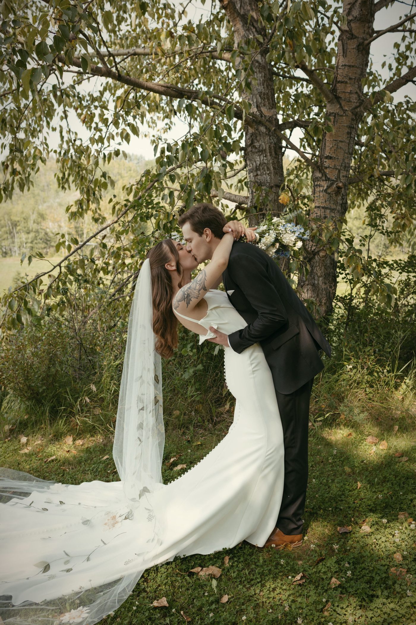 A kiss under the trees, her long veil falling down her back