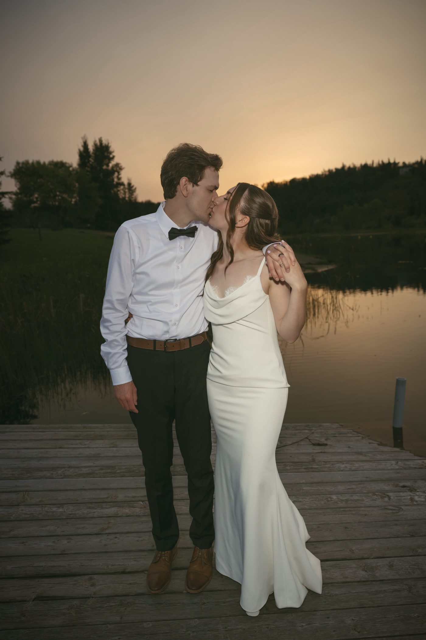 A couple on the dock after sunset, her head on his shoulder, the lake quiet behind them