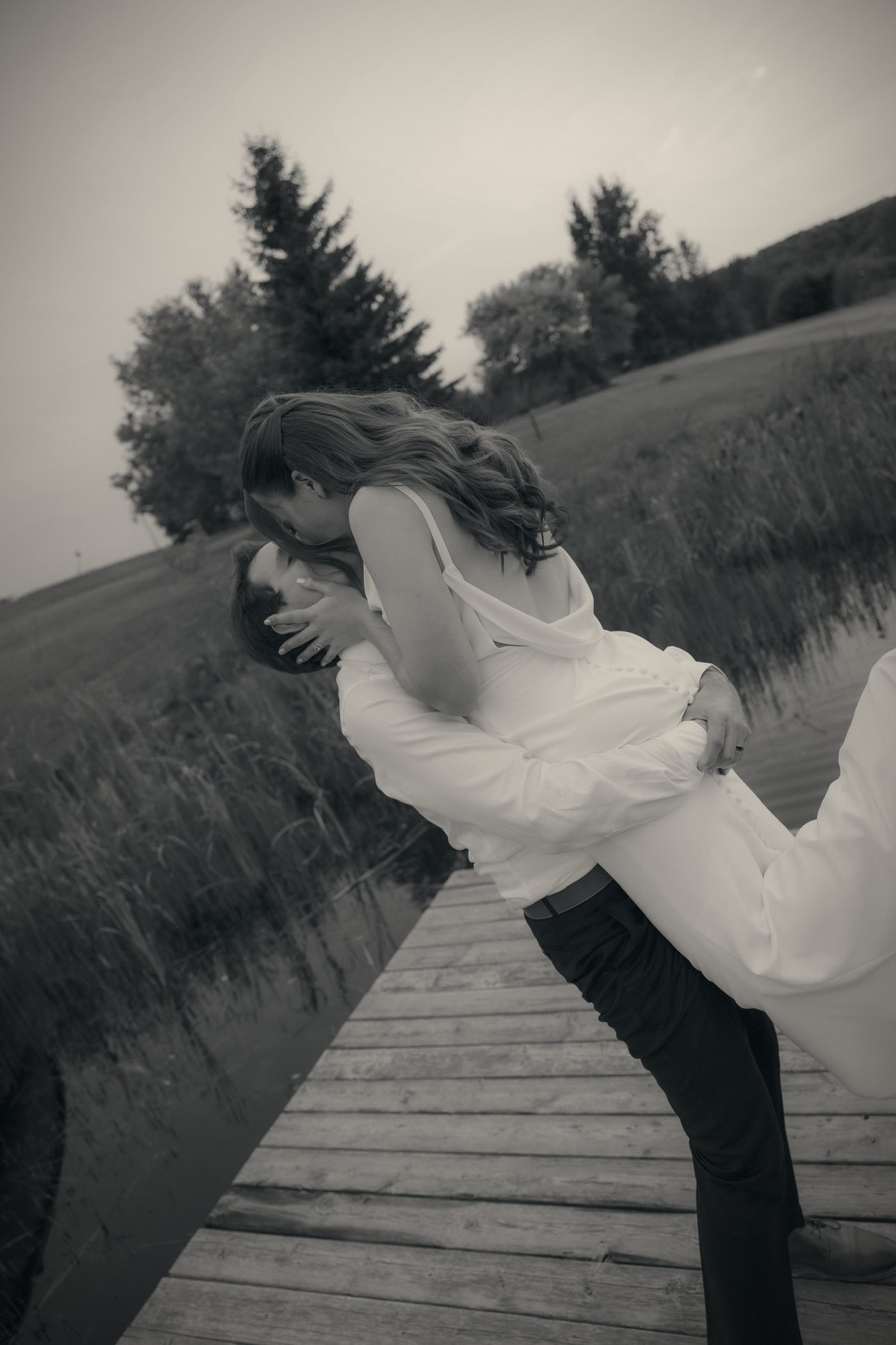 A black and white frame of a couple on the dock, the groom lifting his bride in a kiss