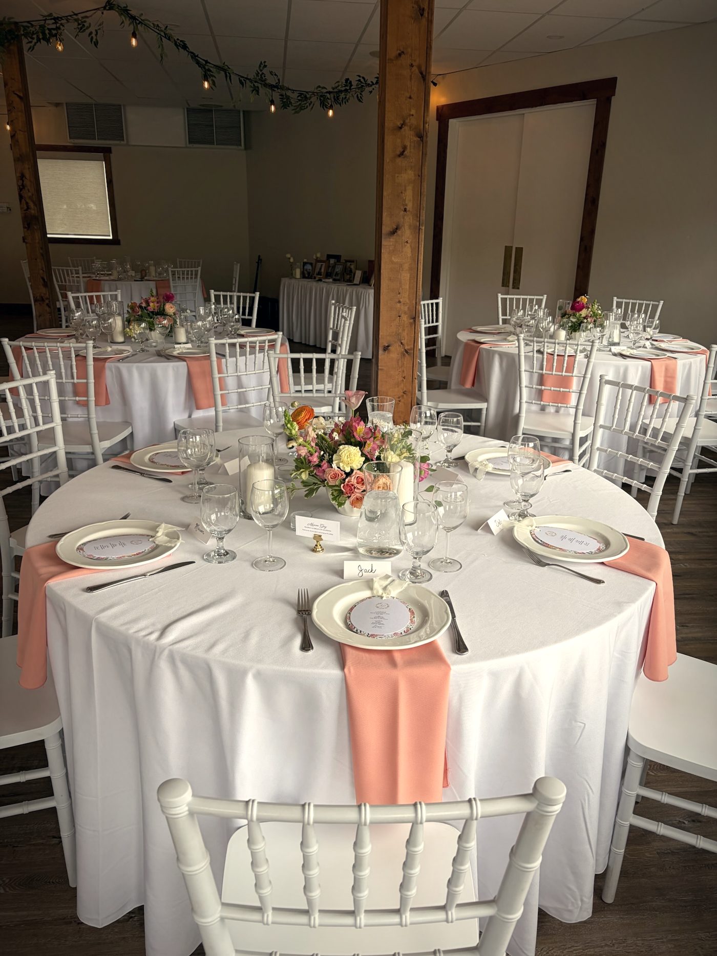 A round table set with white linen, peach napkins and a low floral centrepiece