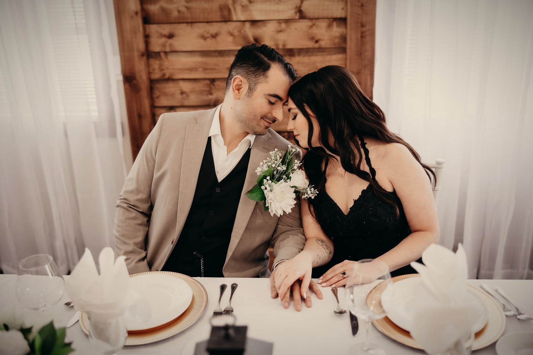 A couple leaning in close at the head table, foreheads together, gold-rimmed plates in front of them