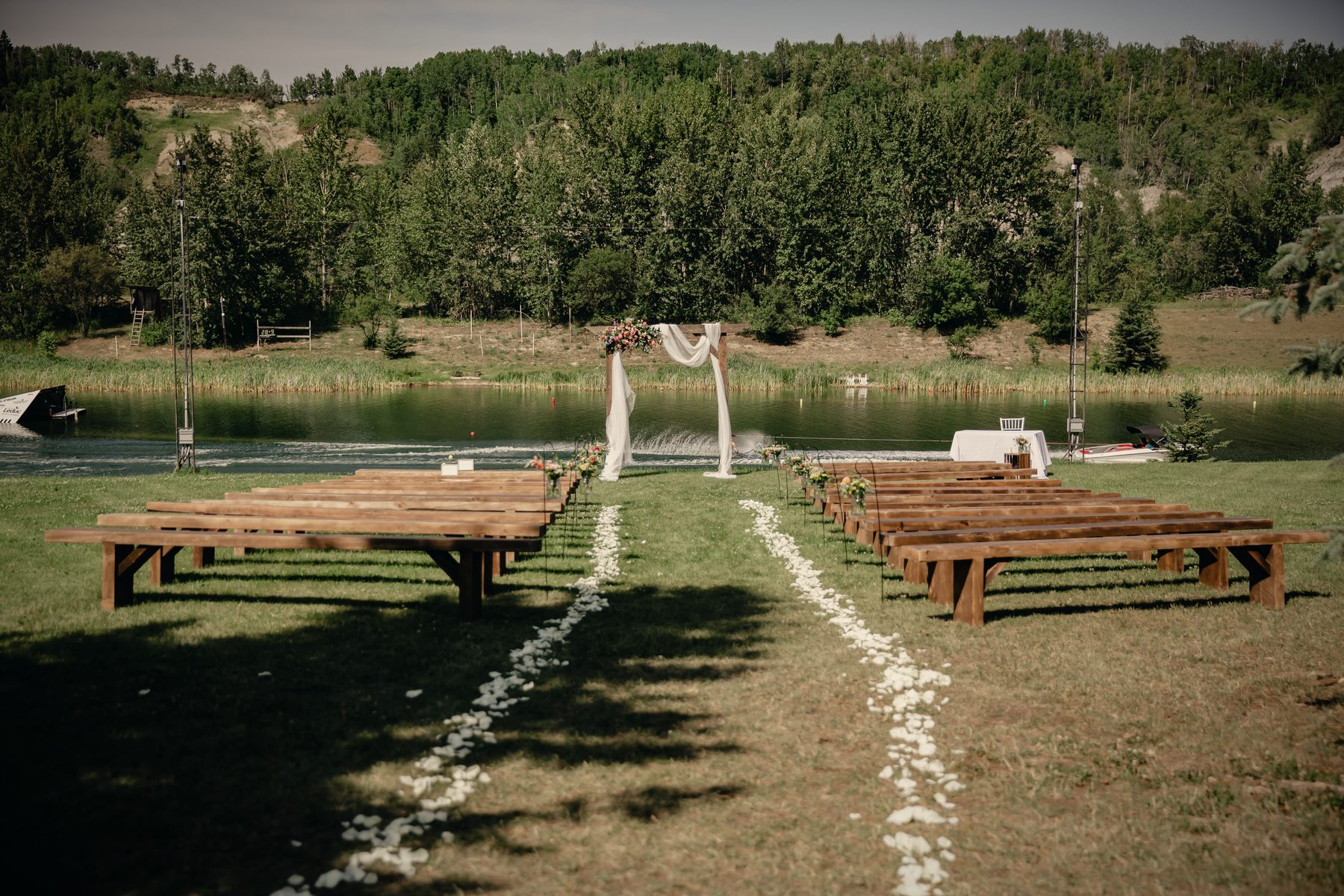 Wooden benches either side of a petal-strewn aisle running to the arbour at the water's edge
