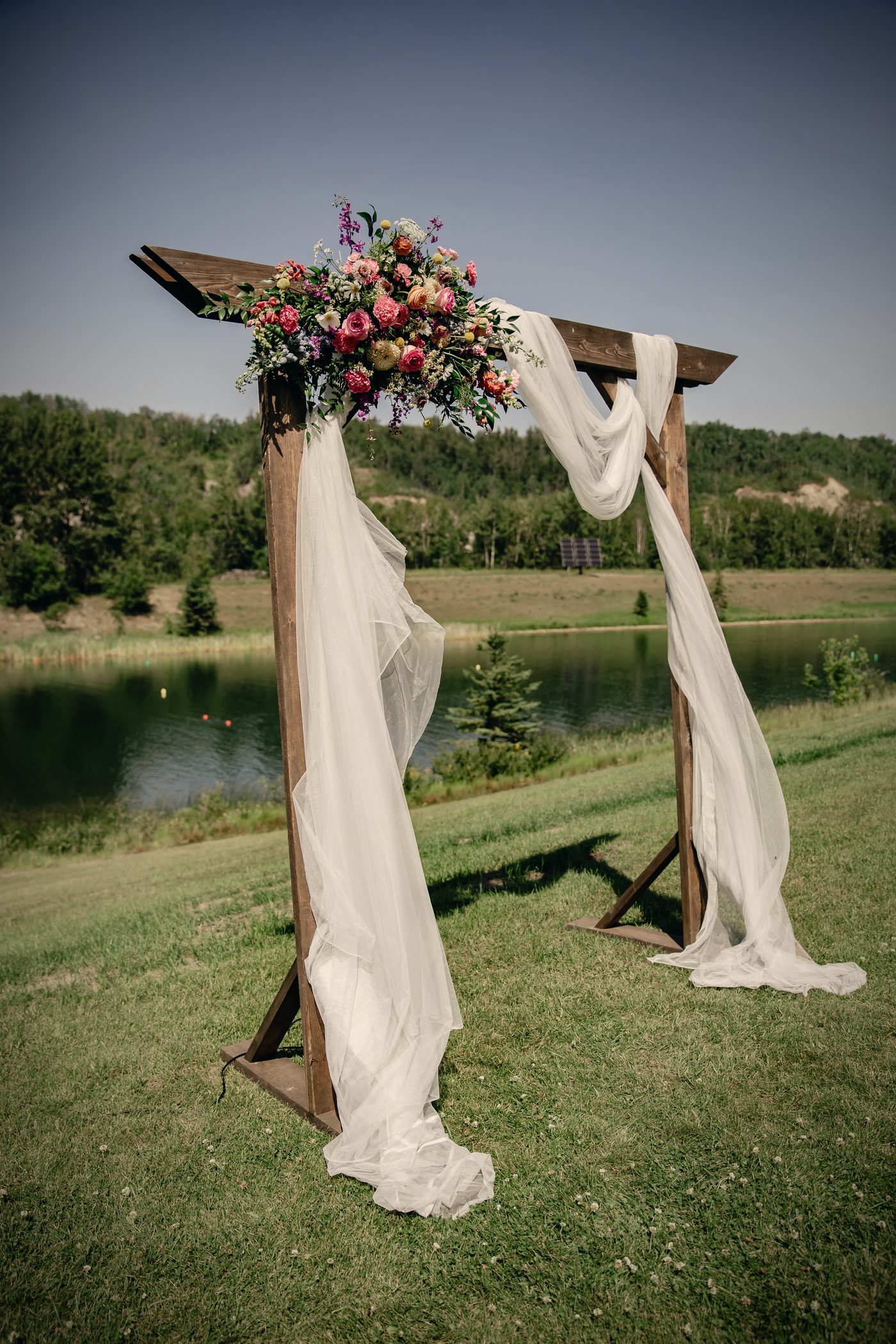 The arbour dressed in florals and white drapery on the lawn, the lake behind it