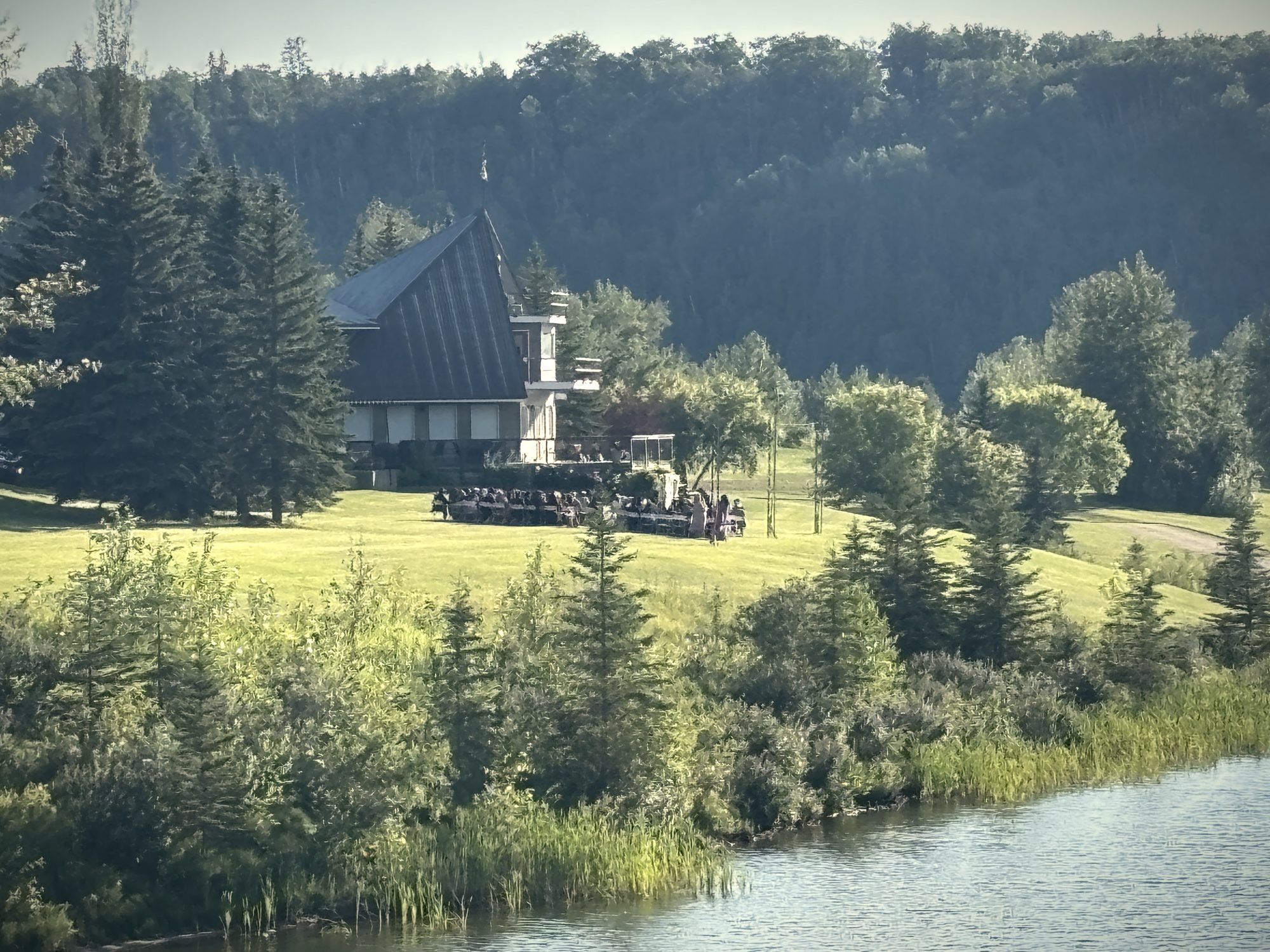 The hall among the spruce above the water, a gathering on the terrace in front of it