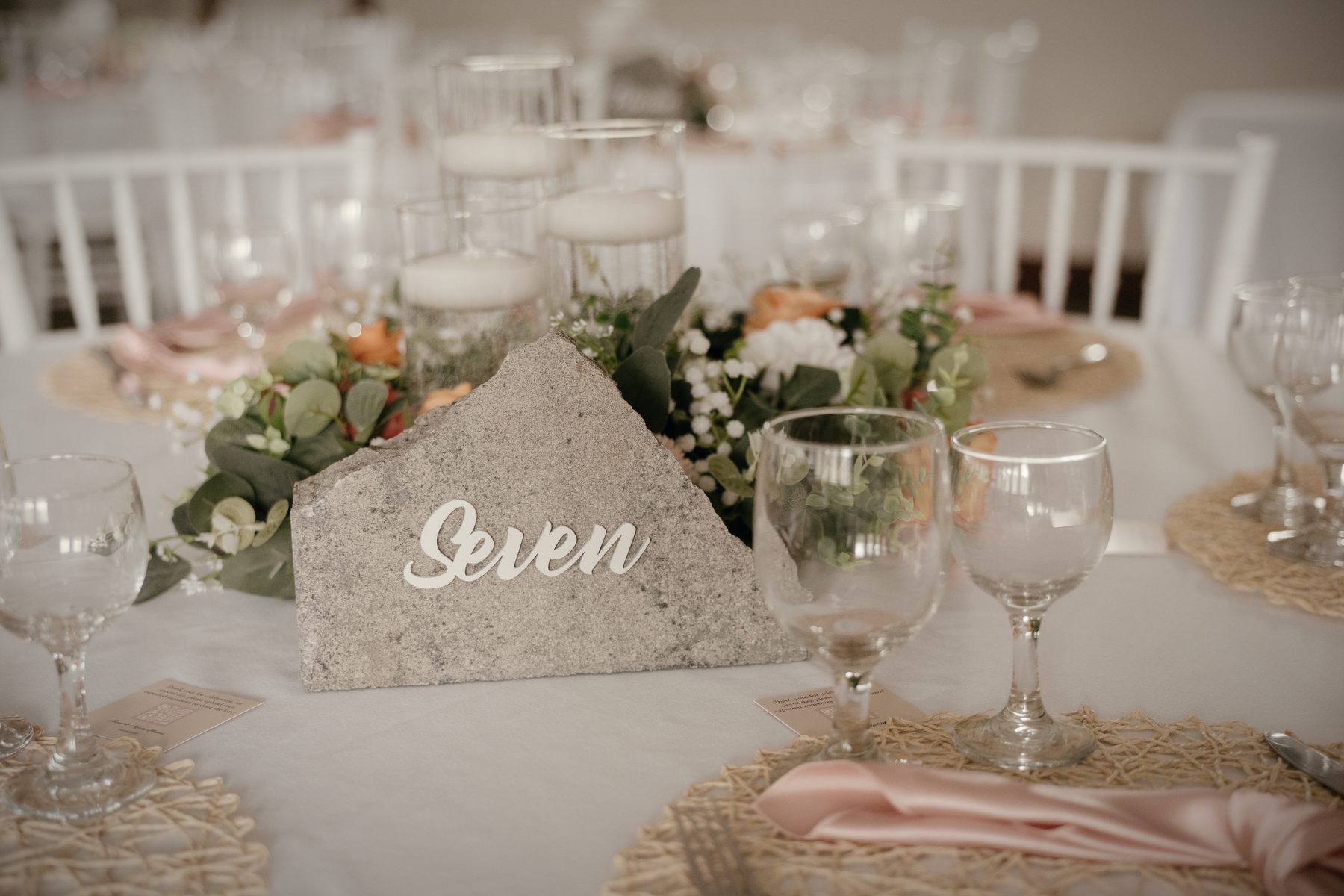 A stone table number reading Seven among roses, with white chairs and the hall blurred behind