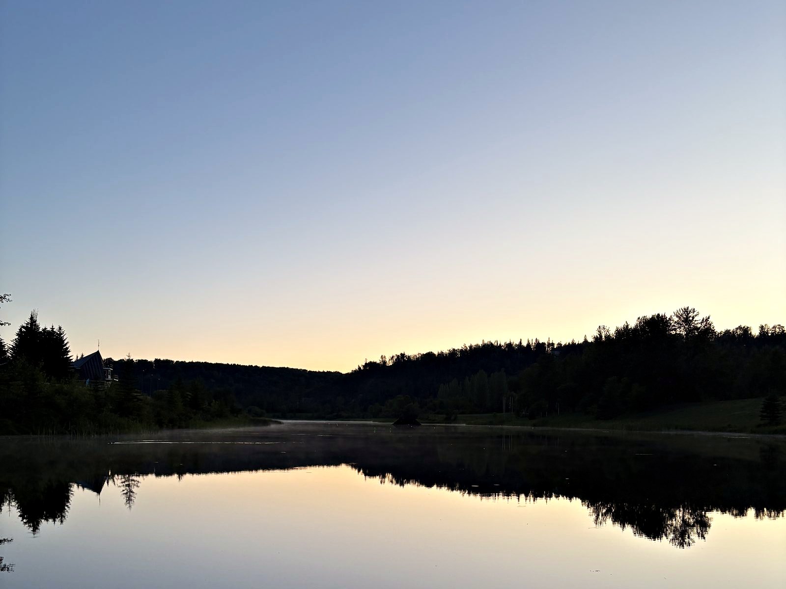 The lake at last light, mist standing on the surface and the treeline doubled beneath it