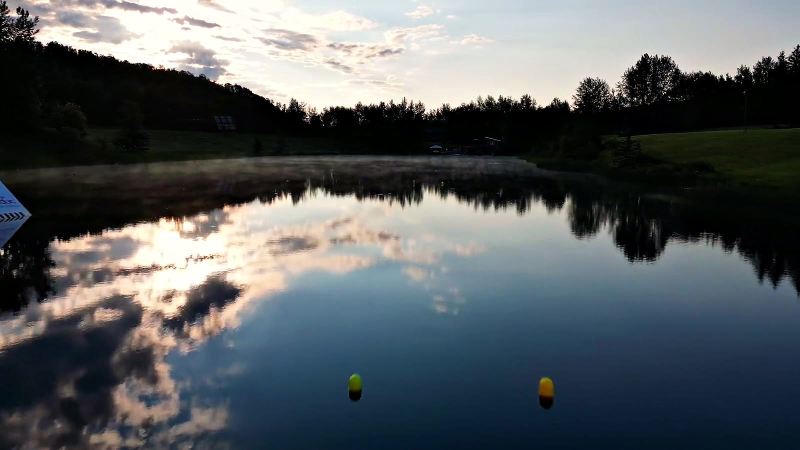 Mist lifting off the lake at dawn, a slalom buoy marking the ski course, the far bank and the whole sky reflected whole