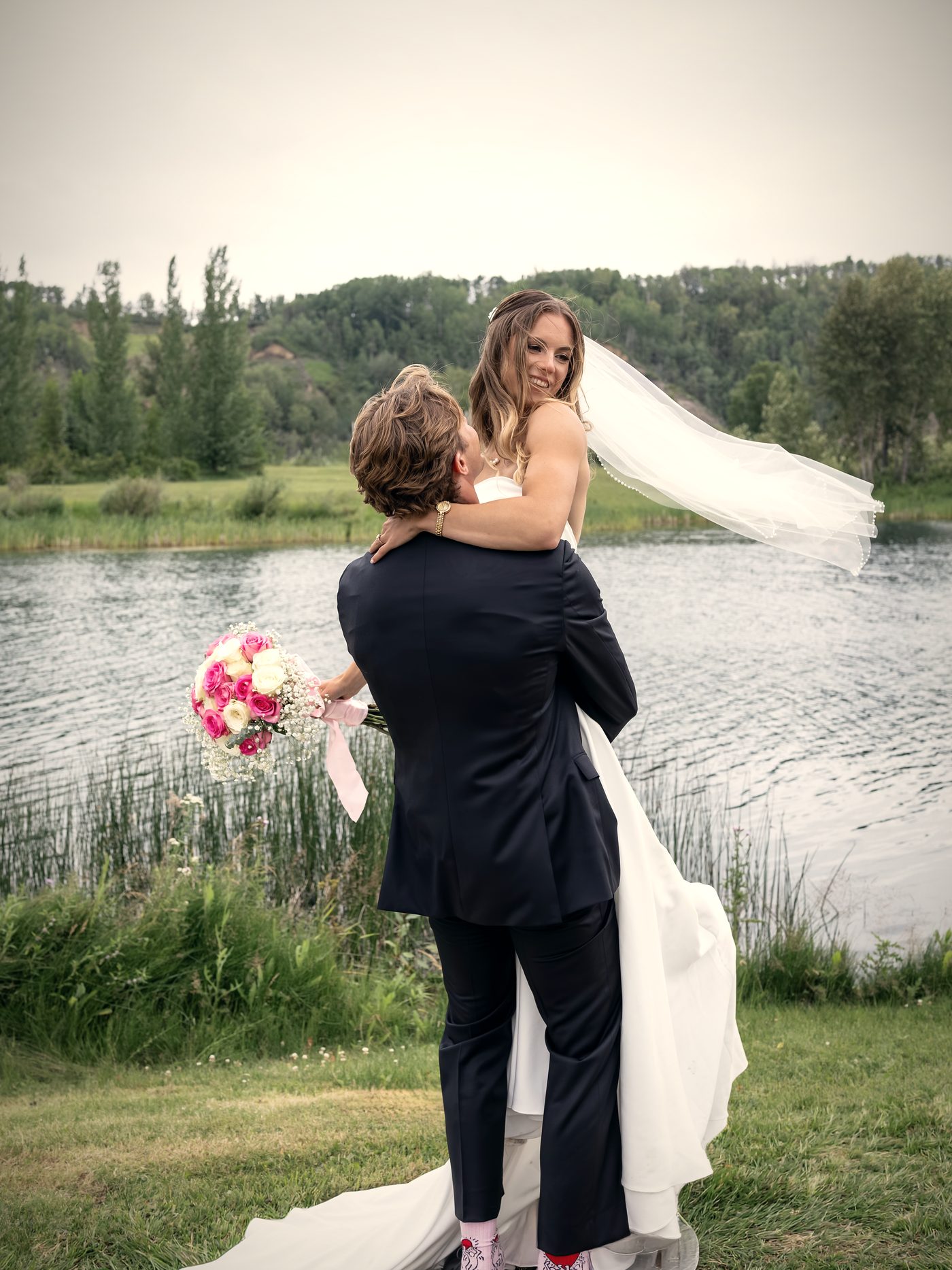 The groom lifting his bride at the water's edge, her veil caught by the wind