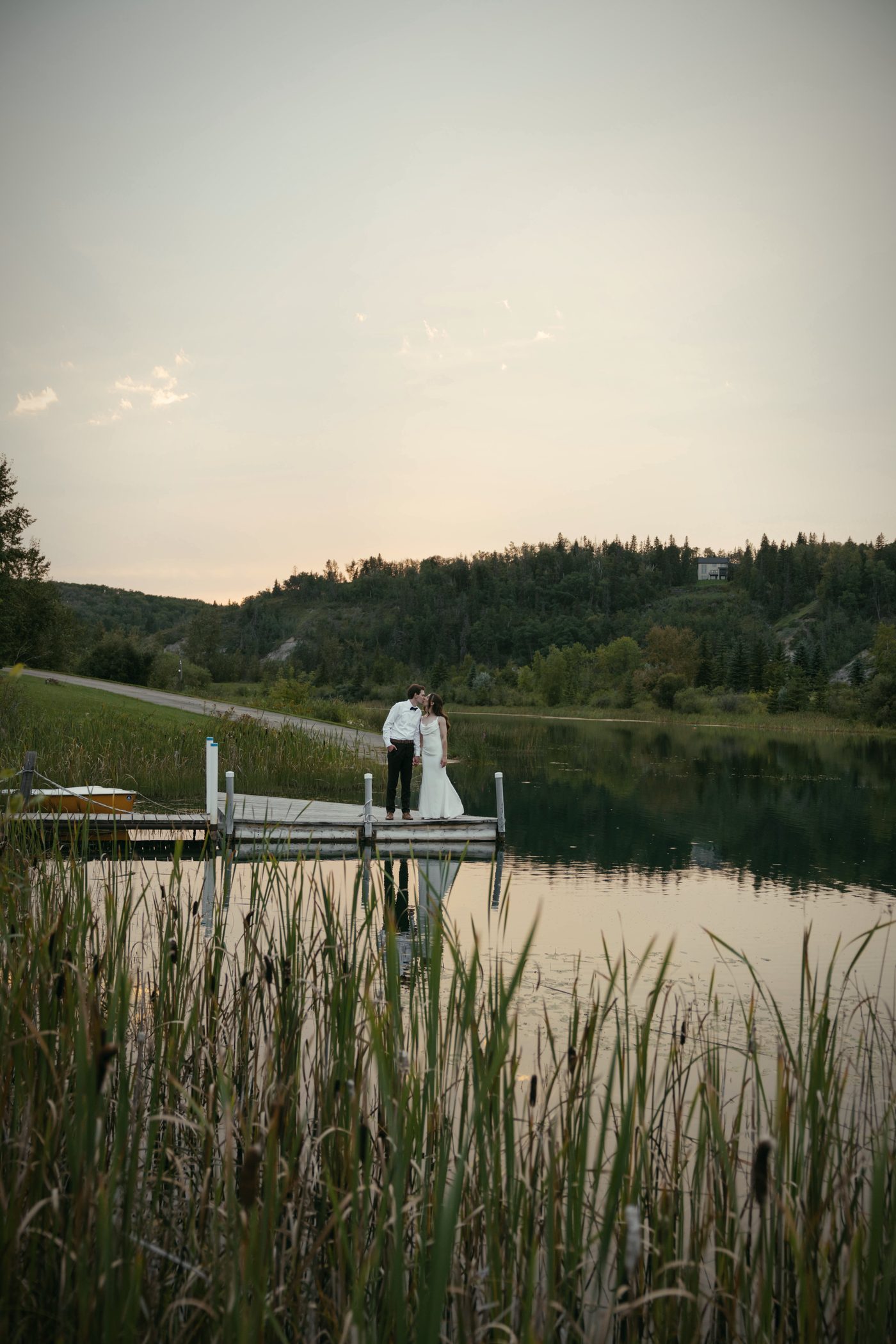Dusk on the lake, a couple standing on the far dock with the reeds in front