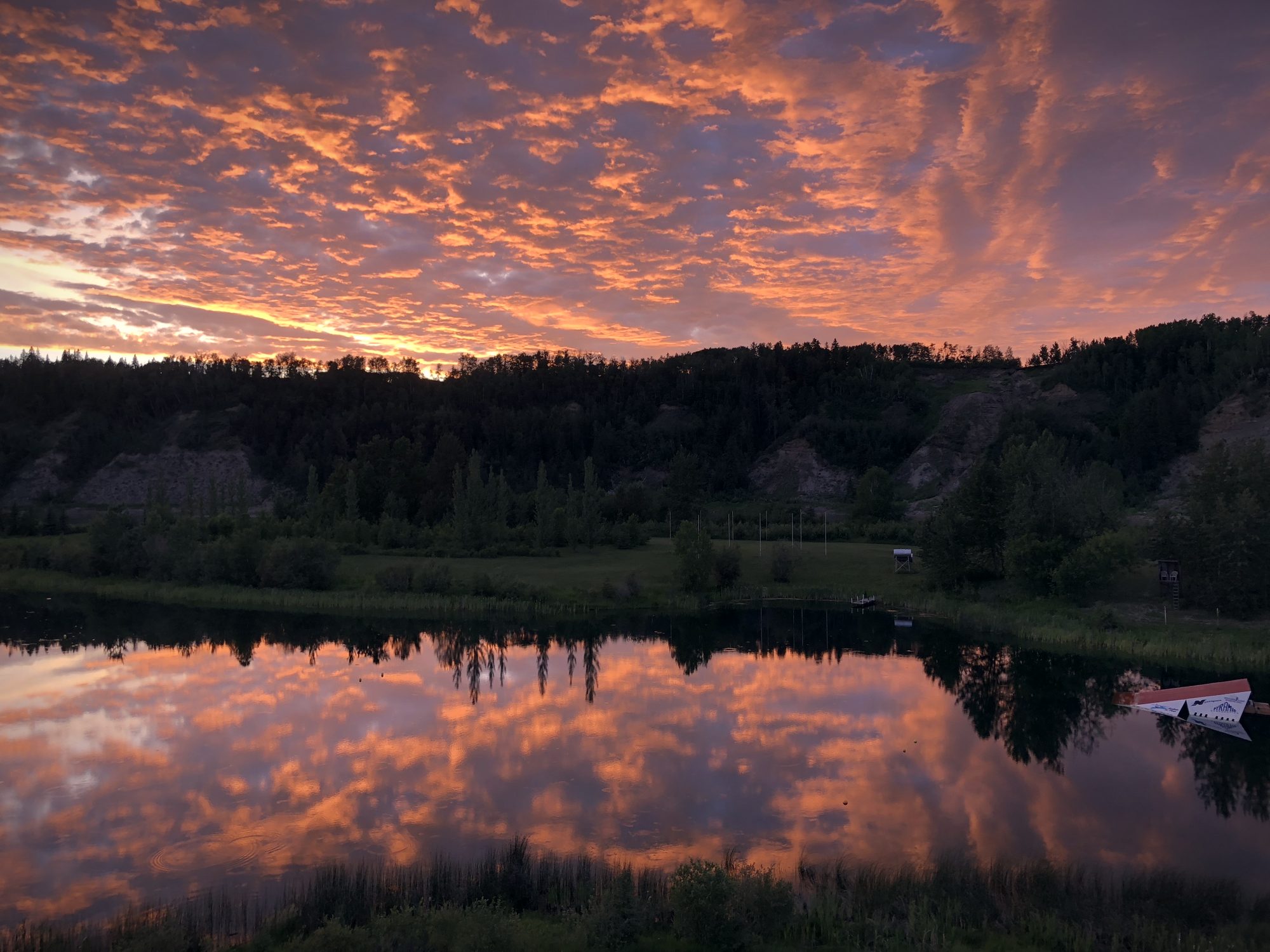 A sunset of orange and violet cloud reflected whole in the lake, the treeline dark beneath it