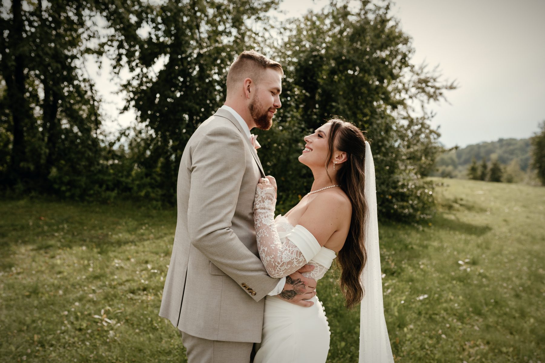 A bride looking up at her groom, smiling, her veil falling behind her on the lawn above the lake